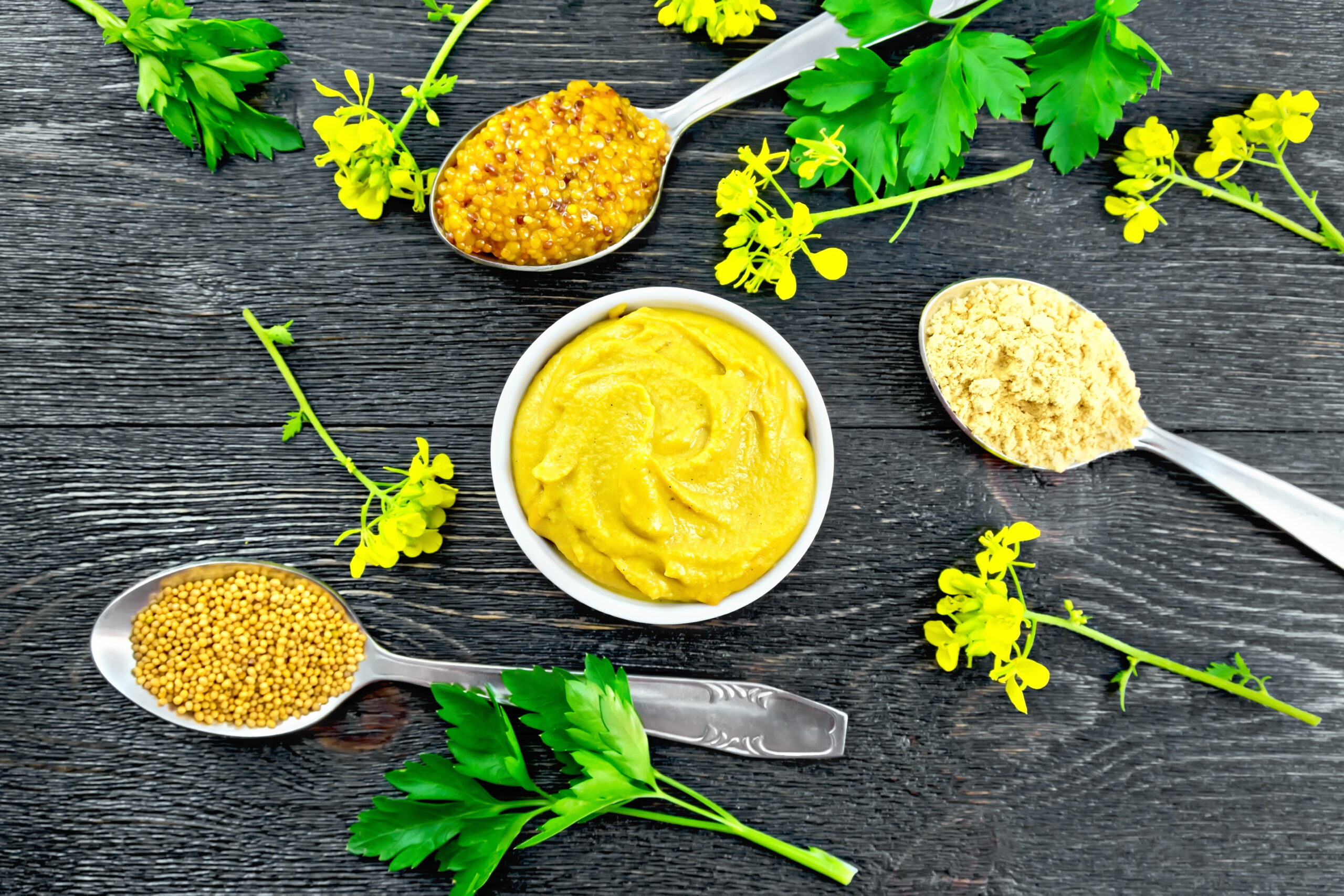 Mustard different in bowl and spoons on board top