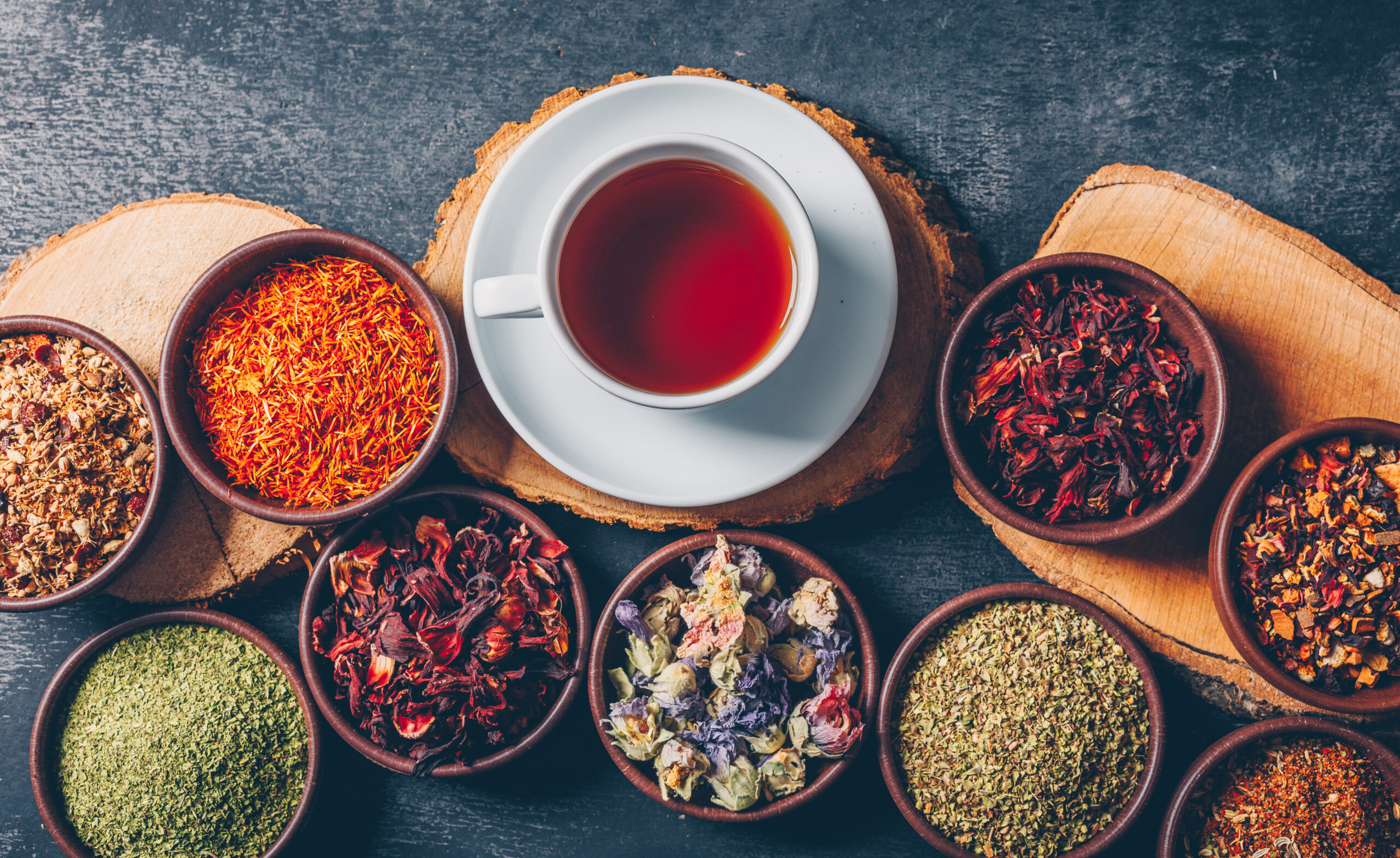 Set of wood stubs and a cup of tea and tea herbs in a bowls on a dark textured background. flat lay